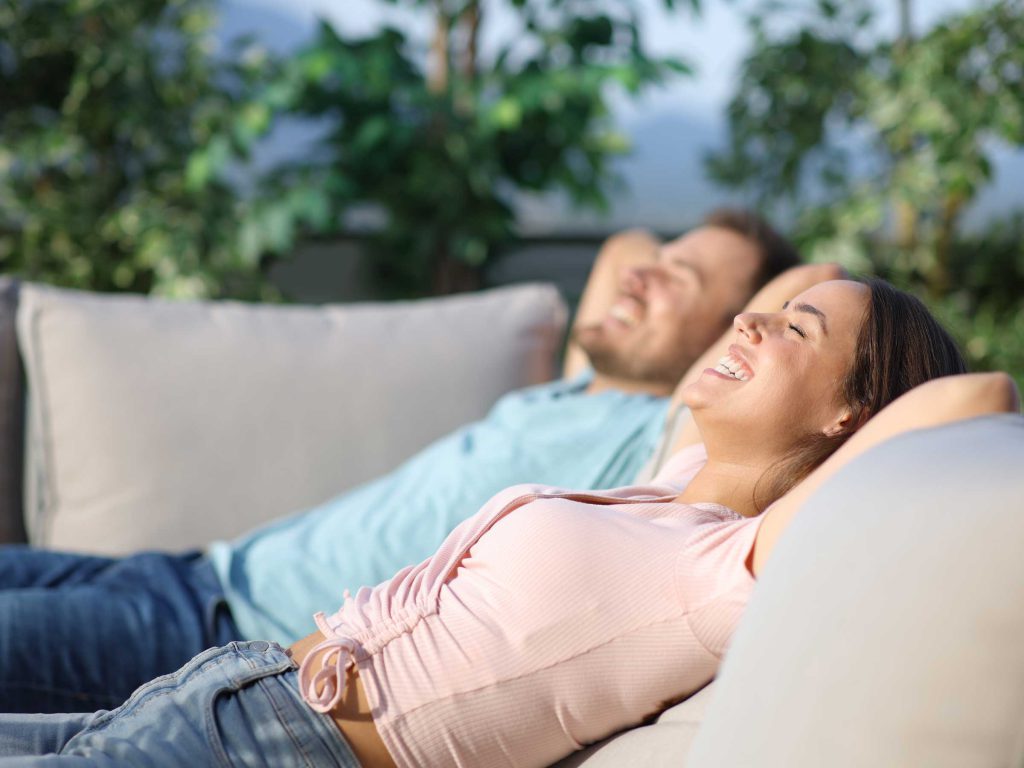 Zwei entspannte Menschen liegen auf einem Sofa im Freien und genießen die Sonne