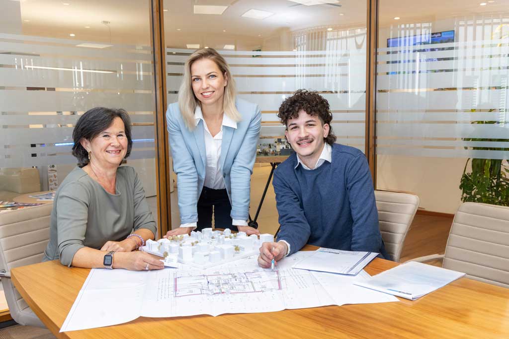 Drei Personen besprechen Architekturpläne und Modell in modernem Büro