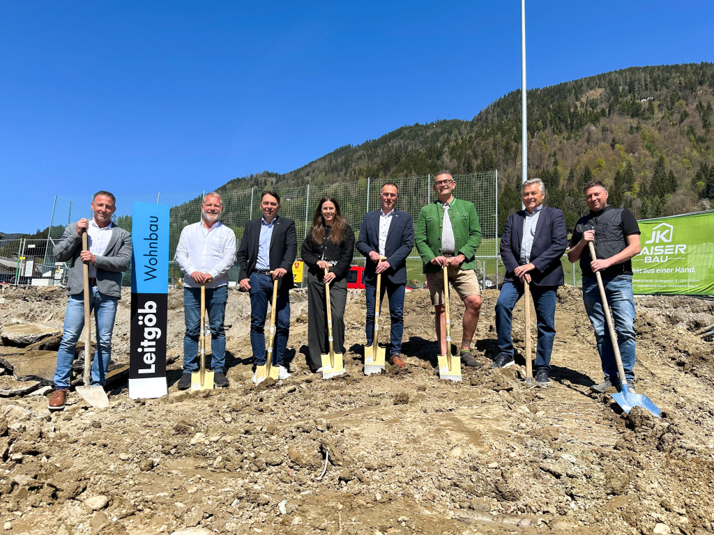 Acht Personen mit Spaten beim Baustart auf einer Baustelle vor Bergkulisse in St. Veit im Pongau