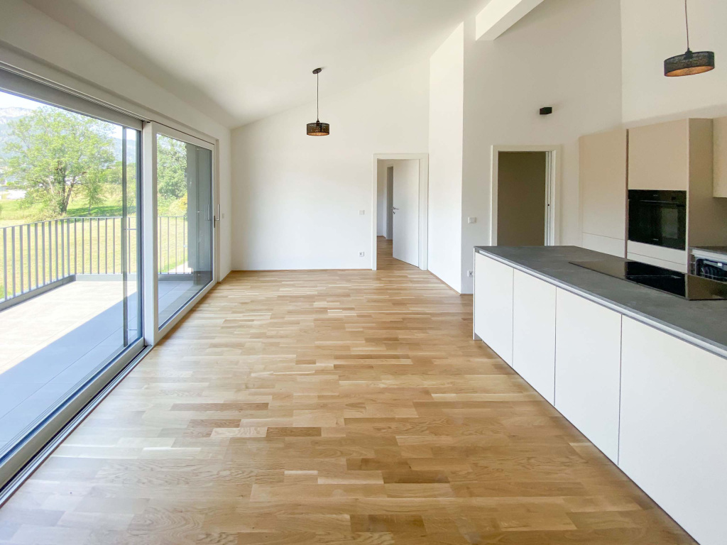 Heller offener Wohnbereich mit weißer Küche, Parkettboden und Balkon mit Blick ins Grüne