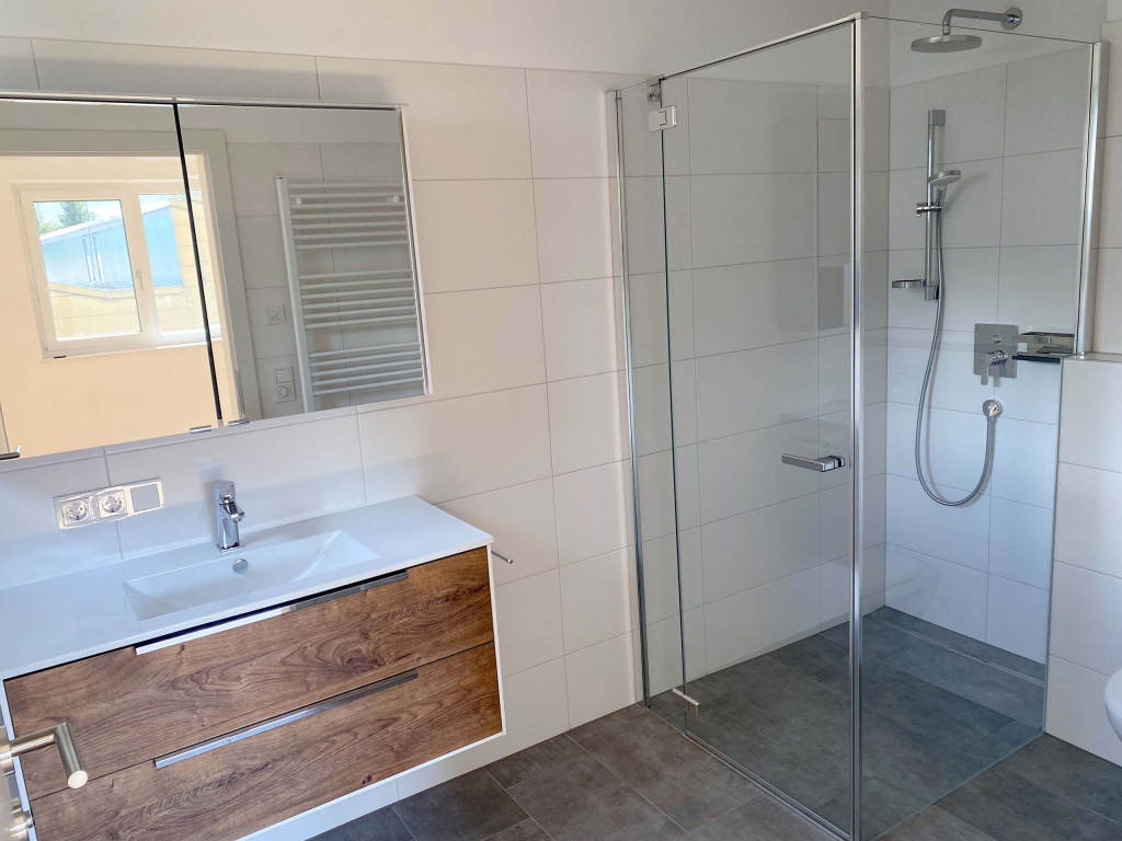 Modernes Bad mit Holzwaschtisch, großem Spiegel und bodengleicher Glasdusche