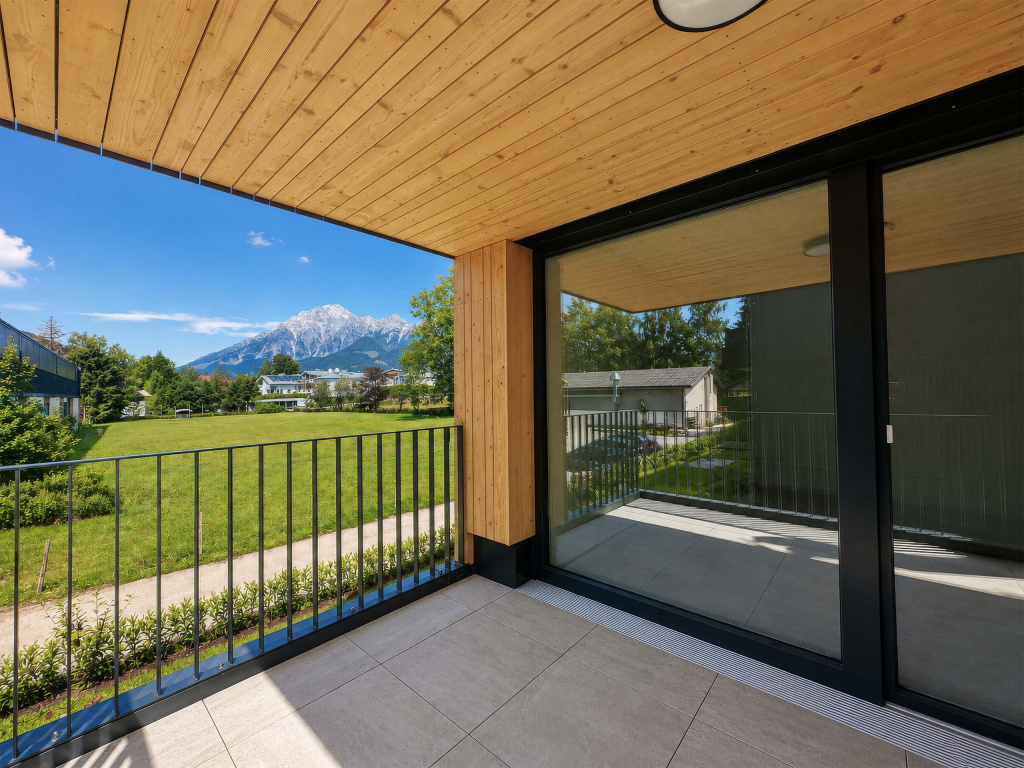 Überdachter Balkon mit Holzdecke und Blick über Wiesen auf ein Bergmassiv
