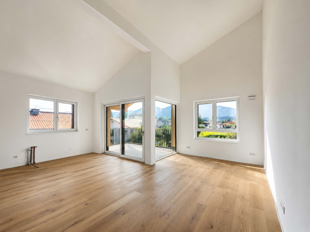 Heller leerer Wohnraum mit hohen Decken, Parkettboden, Balkon und Bergblick
