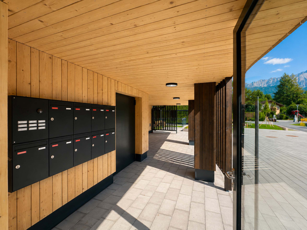 Überdachter Hauseingang mit Holzverkleidung, schwarzen Briefkästen und Blick auf die Berge