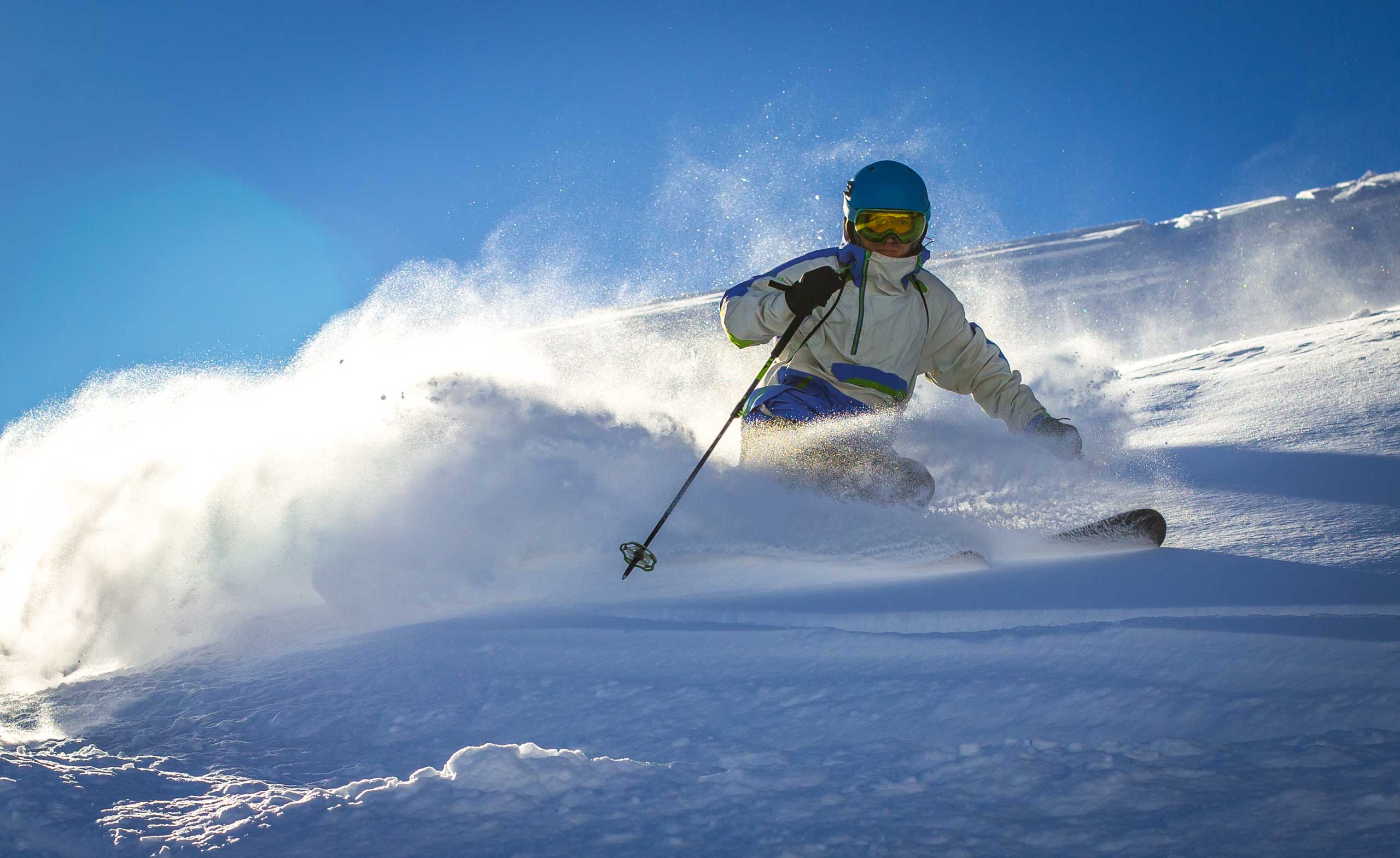 Skifahrer in weißer Jacke fährt durch tiefen Pulverschnee unter blauem Himmel